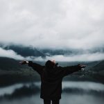 A person enjoys a sense of freedom by a misty mountain lake, embracing nature's tranquility.