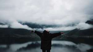 A person enjoys a sense of freedom by a misty mountain lake, embracing nature's tranquility.